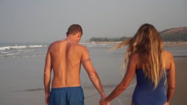 Güzel genç çift deniz kıyısında kumsalda yürüyor.