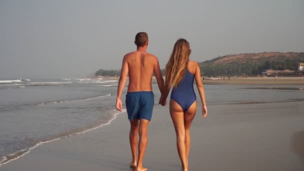 Friss házasok, egy fiatal szerelmespár sétál nyáron a homokos tengerparton. — Stock videók