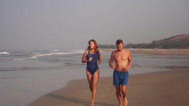 Genç adam ve kadın plaj boyunca koşuyorlar. Sevgili çift denizde koşuyor.