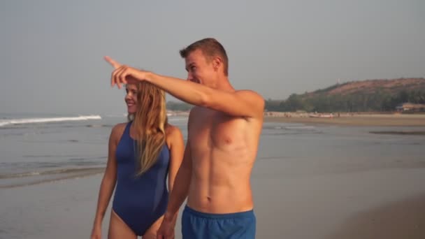 Una joven pareja enamorada pasea por la playa. Un hombre y una mujer caminan sobre el mar — Vídeos de Stock