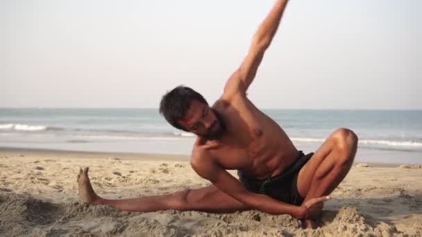 En man utövar yoga på morgonen på en tom sandstrand — Stockvideo