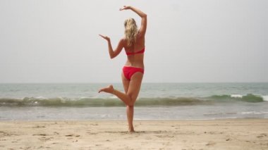 Güzel genç bir kadın deniz kenarındaki kumlu bir plajda yoga yapıyor.