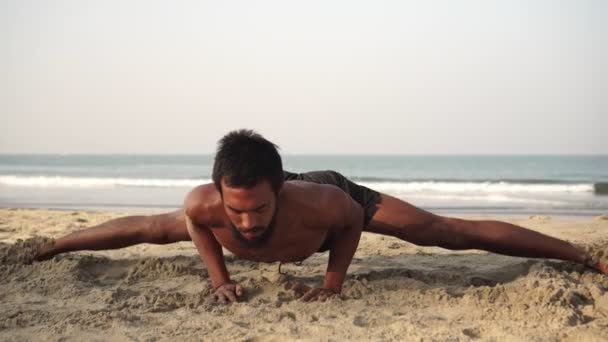 Un uomo pratica yoga su una spiaggia di sabbia. Uno yogi maschio siede su uno spago — Video Stock