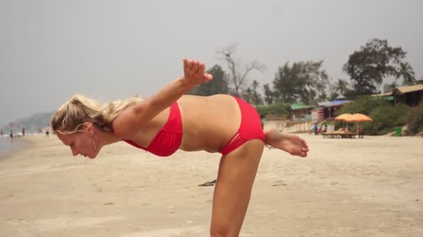 Όμορφη νεαρή γυναίκα με μαγιό κάνει γιόγκα στην παραλία. — Αρχείο Βίντεο