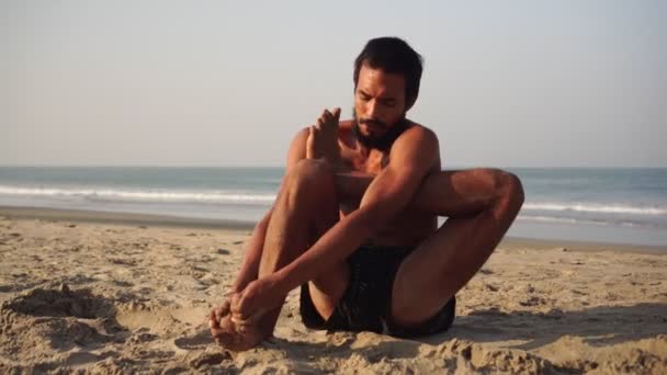 Un giovane uomo pratica yoga sulla spiaggia sullo sfondo del mare — Video Stock