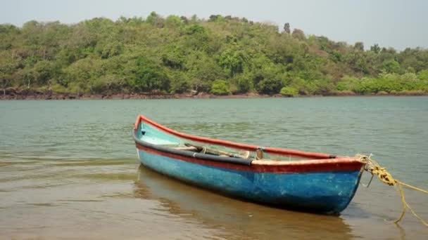 Antiguo barco de madera en la orilla de un río tropical. Un barco pesquero de madera se balancea sobre las olas — Vídeo de stock