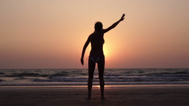 Молодая женщина занимается спортом на пляже на фоне заката — стоковое видео