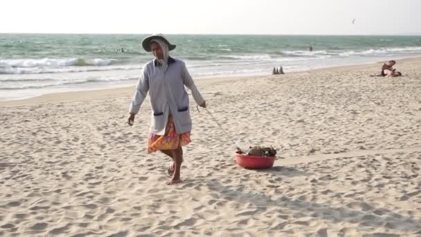 Arambol, Ινδία - Φεβρουάριος 2020. Γυναίκα καθαρότερο στην παραλία με ένα καλάθι με σκουπίδια — Αρχείο Βίντεο