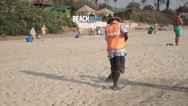 Arambol, Ινδία - Φεβρουάριος 2020. Ένας σκουπιδιάρης μαζεύει σκουπίδια στην παραλία. — Αρχείο Βίντεο