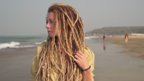 Uma jovem hippie mulher com dreadlocks está andando ao longo de uma praia de areia — Vídeo de Stock