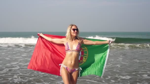 Fiatal nő portugál zászlóval a tengerparton, lassított felvétel. Turizmus Portugáliában