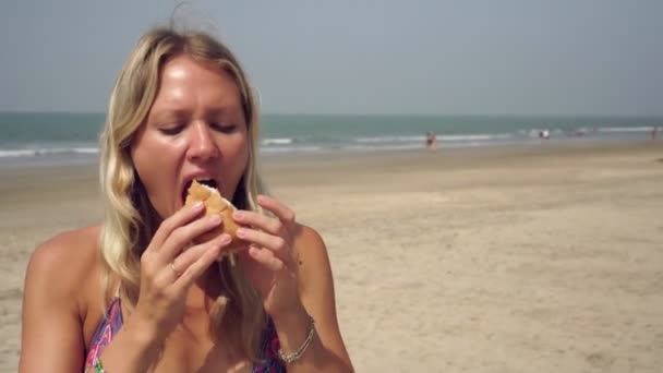 Retrato de una mujer que come una hamburguesa. Chica comiendo comida rápida, una hamburguesa en la playa — Vídeo de stock