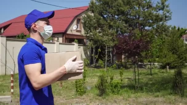 Egy férfi orvosi maszkban és kesztyűben kartondobozt hord. — Stock videók