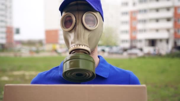 Portrét doručovatele v plynové masce nebo respirátoru s lepenkovou krabicí na ulici. — Stock video
