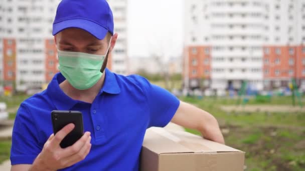Delivery man σε μια προστατευτική ιατρική μάσκα στο πρόσωπό του χρησιμοποιεί ένα smartphone — Αρχείο Βίντεο