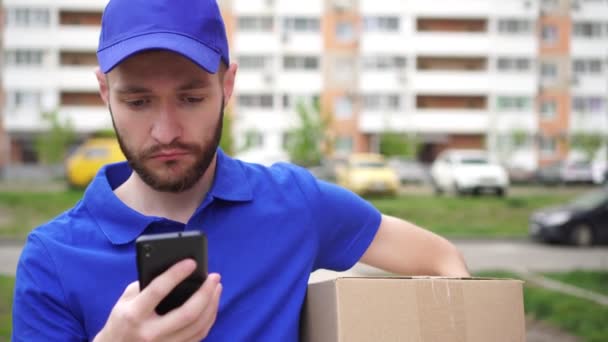 Courier delivery man met een pakket is op zoek naar de smartphone — Stockvideo