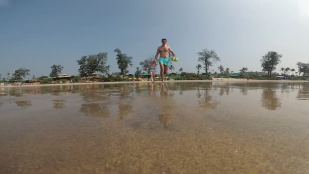 Um jovem pai masculino corre com uma menina em uma praia molhada. Família no mar — Vídeo de Stock