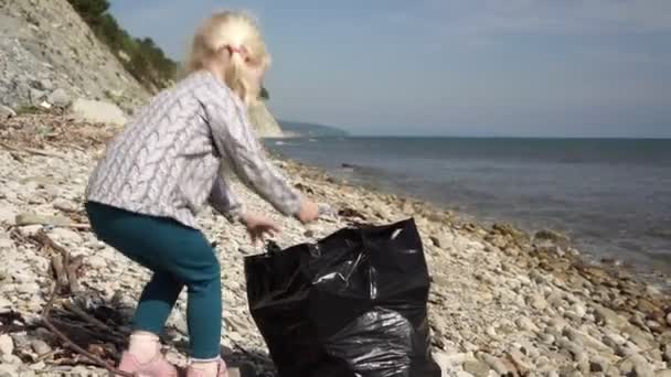 Kind meisje helpt bij het schoonmaken van afval en plastic afval op de kust — Stockvideo