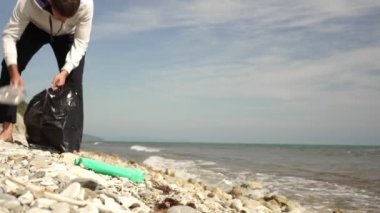Gönüllü bir adam çöpleri temizler ve plajdaki plastik atıkları temizler.