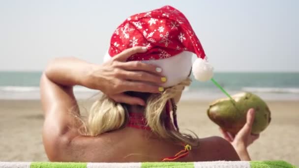 Молодая женщина в шляпе Сантас празднует Рождество или Новый год на тропическом морском пляже — стоковое видео