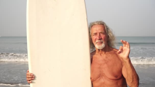 Een oudere volwassen man een oude man met een surfplank toont een teken ok — Stockvideo