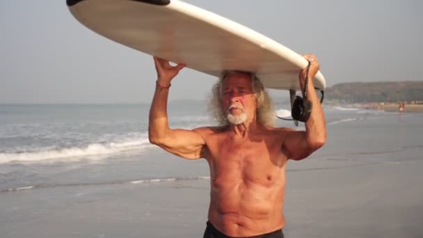 O velho avô saudável e forte vai com uma prancha de surf. Cidadão idoso com surfe — Vídeo de Stock