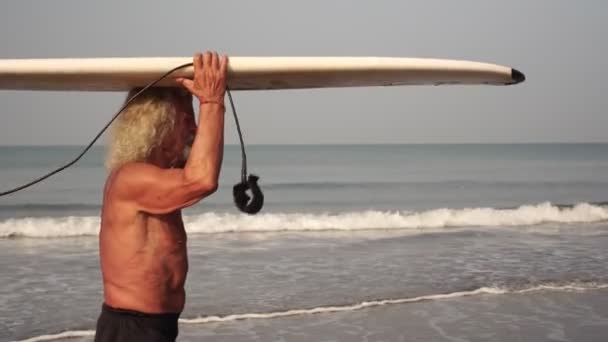 Gray-haired old man grandfather at sea with a surfboard. Mature male surfer — Stock Video