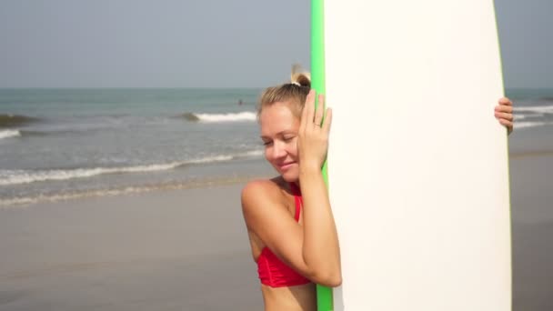 Retrato de uma jovem atraente com uma prancha de surf em um dia ensolarado na praia . — Vídeo de Stock