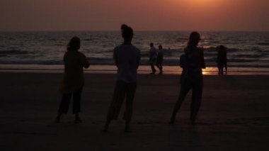 Arambol, Hindistan - Şubat 2020. Gün batımında plajda yoga yapan bir grup insan. İnsanlar qigong egzersizleri yapar..