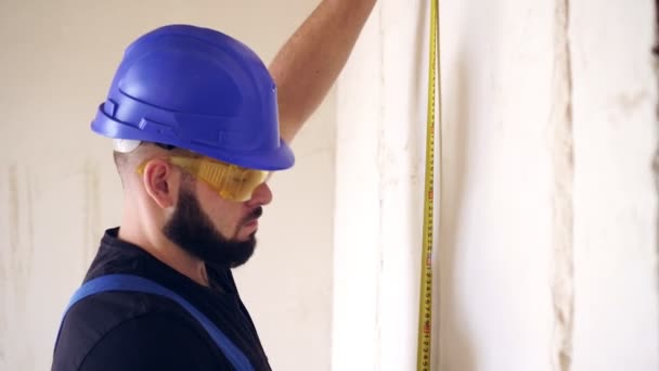 Un constructor de sex masculin măsoară peretele cu o măsură de bandă de construcție — Videoclip de stoc