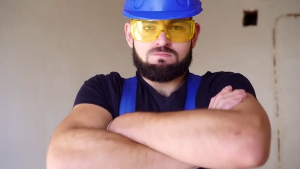 Retrato de un joven constructor fuerte en uniforme de trabajo. Trabajador en una obra de construcción — Vídeos de Stock