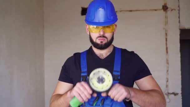 Мужчина-строитель с угловой мельницей. Портрет рабочего на строительной площадке с инструментом — стоковое видео