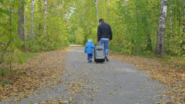 Чоловік і дитина з валізою, що йде лісовою дорогою — стокове відео