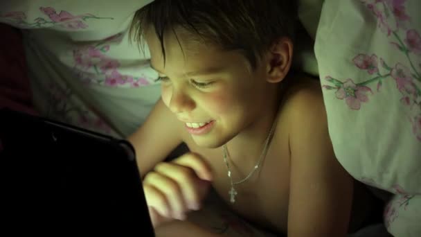 Мальчик лежит под одеялом и смотрит мультики на сенсорной панели — стоковое видео