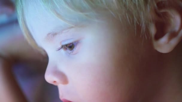 Мальчик лежит под одеялом и смотрит мультики на сенсорной панели крупным планом лицо — стоковое видео