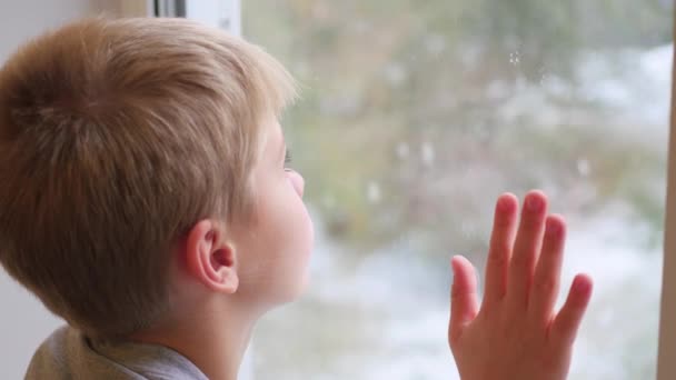 Seorang anak melihat keluar jendela saat salju turun — Stok Video