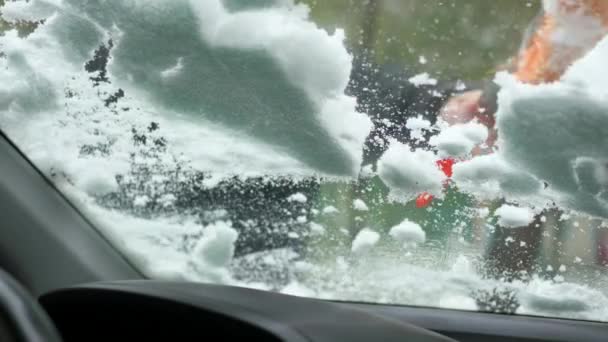 Парень убирает снег из окна заснеженной машины — стоковое видео