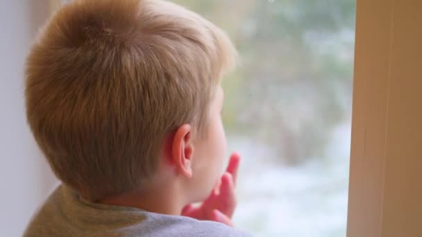 Ett barn ser ut genom fönstret på snöfallet — Stockvideo