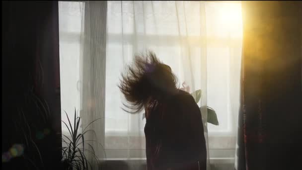 Девушка весело танцует у окна под солнцем — стоковое видео