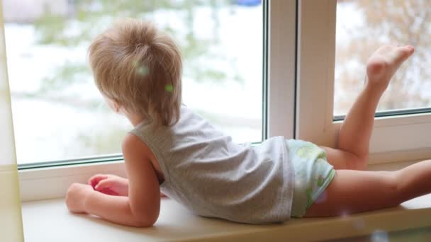 El niño mira por la ventana — Vídeo de stock