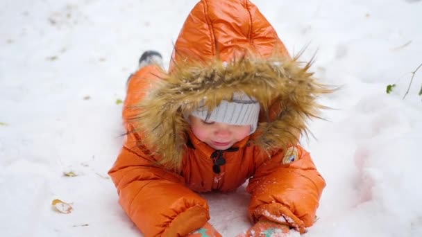 Счастливый ребенок лежит на снегу и улыбается — стоковое видео