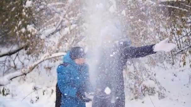 Το κορίτσι και το παιδί ρίχνει χιόνι πάνω από τον εαυτό του και το απολαμβάνει στο χειμερινό πάρκο — Αρχείο Βίντεο