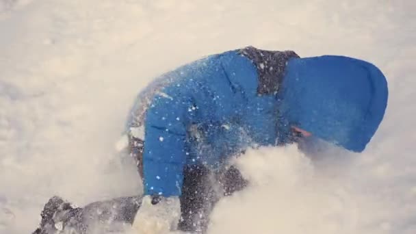 Niño rueda la cabeza sobre los talones con la colina en la nieve — Vídeos de Stock