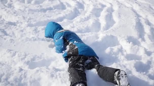 Niño rueda la cabeza sobre los talones con la colina en la nieve — Vídeo de stock