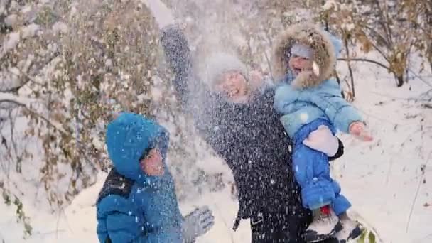 Το κορίτσι και το παιδί ρίχνει χιόνι πάνω από τον εαυτό του και το απολαμβάνει στο χειμερινό πάρκο — Αρχείο Βίντεο