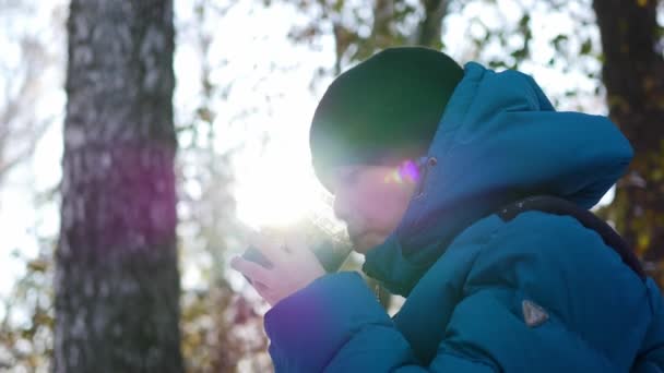 El niño está bebiendo té caliente de una taza en el invierno al aire libre. Día soleado — Vídeos de Stock