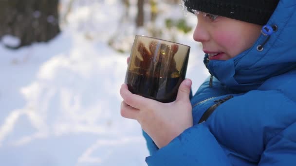 Дитина п'є гарячий чай з чашки взимку на відкритому повітрі. Сонячний день — стокове відео