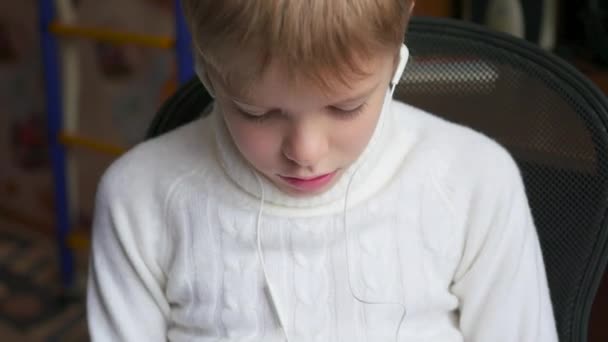 El niño escucha música en el teléfono inteligente en los auriculares y salta de cabeza en casa — Vídeos de Stock