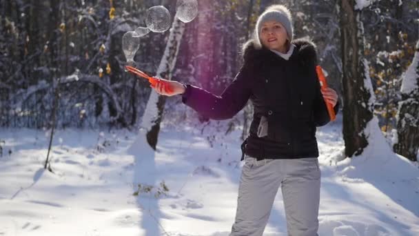 Menina faz grandes bolhas de sabão com prazer no parque de inverno em um dia ensolarado — Vídeo de Stock