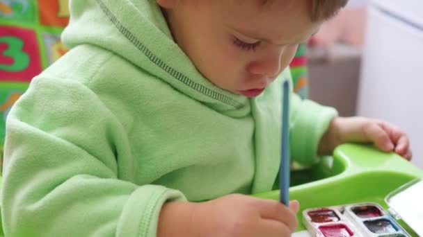 Счастливый ребенок рисует кистью на бумаге — стоковое видео
